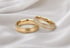 Zwei goldene Eheringe auf weißem Seidenstoff, ein Ring mit Diamanten besetzt und einer mit mattierter Oberfläche.