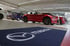 Blauer Teppich mit weißem Mazda-Logo im Autohaus, rote Mazda-Sportwagen im Hintergrund.