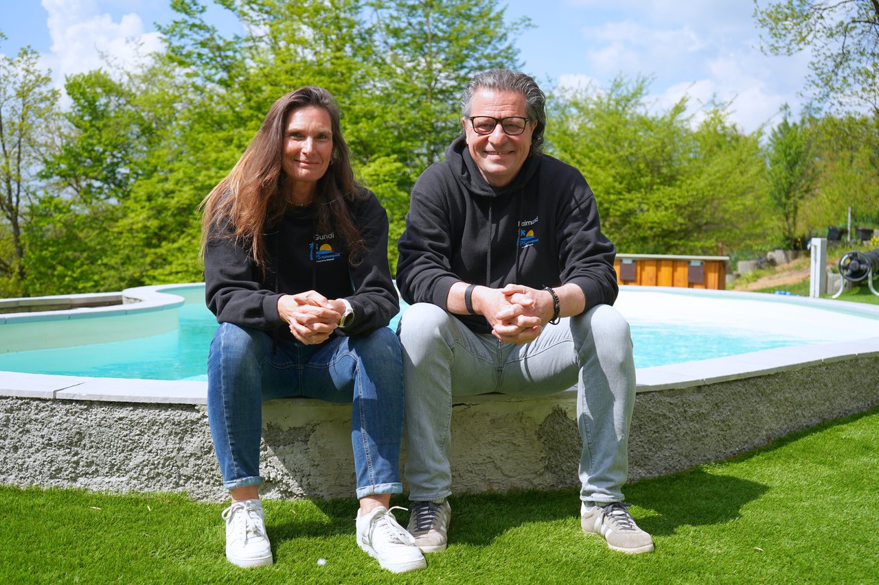 Gundi Poch und Raimund Schmauder sitzen lächelnd am Rand eines Pools im Garten.