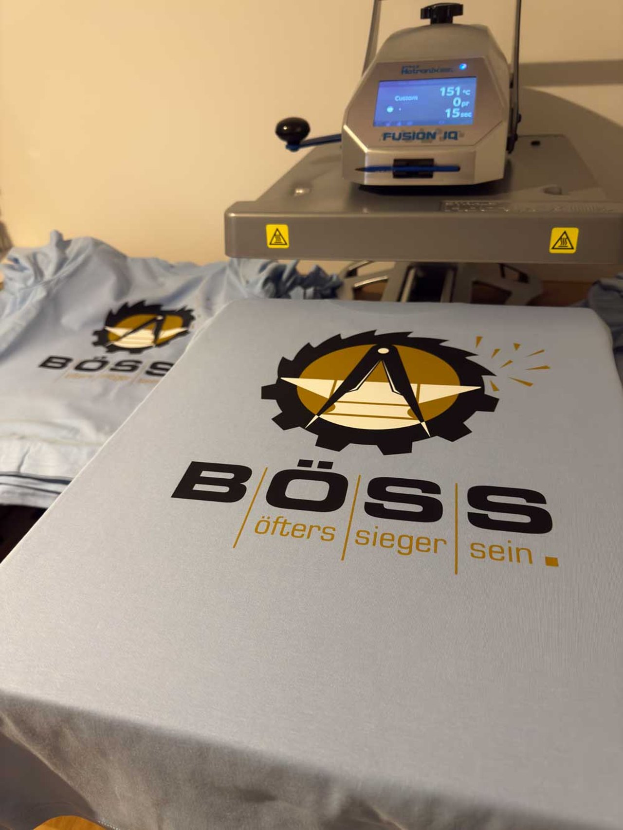 Transferpresse druckt ein Firmenlogo auf ein hellblaues T-Shirt