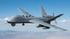 Grauer Militär-UAV mit Propeller am Heck und zwei Raketen unter den Flügeln fliegt über Berglandschaft.