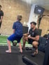 Ein Personal Trainer hilft einem jungen Jungen bei Kniebeugen mit einer Kettlebell in einem Fitnessstudio.