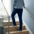 A person in a light blue sweater and navy pants walks up wooden stairs while holding a metal handrail.
