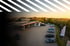 Tankstelle mit mehreren Zapfsäulen und geparkten Autos bei Sonnenuntergang, mit schrägen Linien im oberen Bereich.