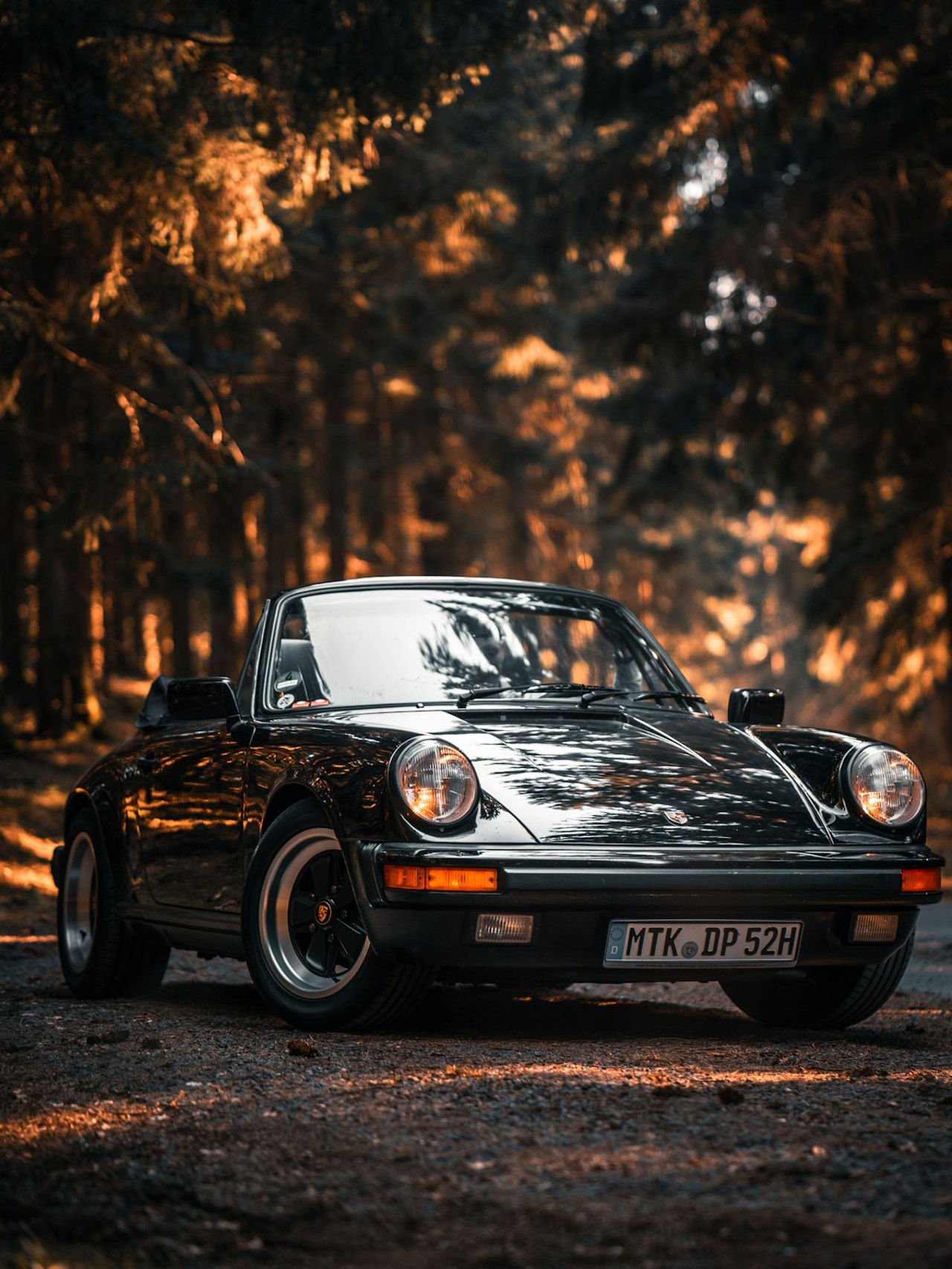 Schwarzer Porsche 911 auf einer Wald-Landstraße als Sinnbild für Fahrzeuge der Extraklasse