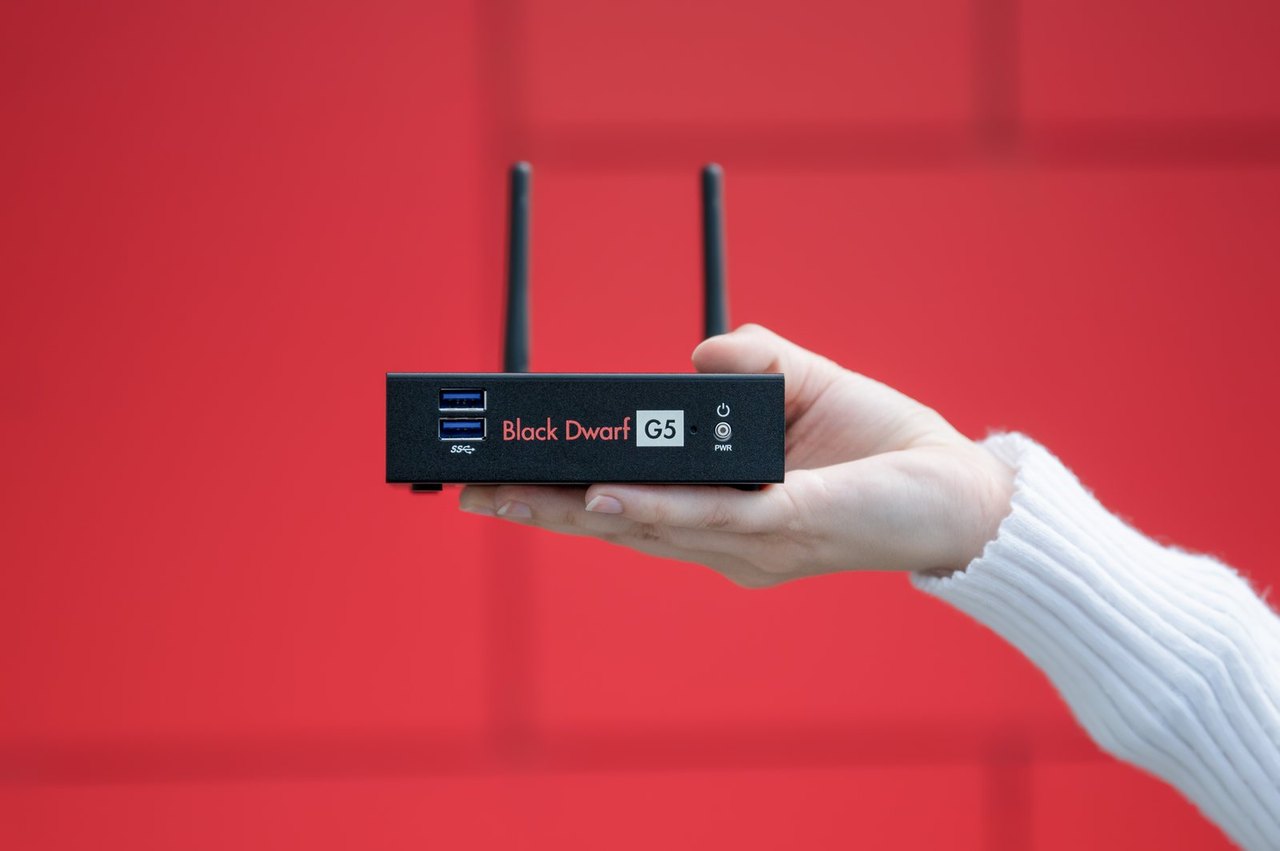 Hand hält eine kleine schwarze Firewall Securepoint Black Dwarf G5 mit zwei Antennen vor einer roten Wand