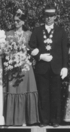Eine Frau im Kleid mit Blumen und ein Mann in Uniform mit Medaillen stehen nebeneinander.