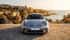 Silver Porsche 911 GT3 parked on a stone patio overlooking the ocean with a sunset sky.