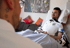 Ein lächelnder Mann im Deutschland-Trikot, mit Beatmungsgerät im Bett, blickt einen anderen Mann an.