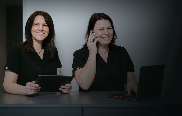 Zwei Mitarbeiterinnen der Praxis an der Anmeldung mit Tablet und Telefon