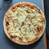 Eine runde Pizza mit geschmolzenem Käse, Zwiebelringen und Tomatensauce auf einem dunklen Tisch von oben fotografiert.