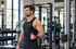 AI Generated: Ein Mann mit schwarzem Tanktop steht im Fitnessstudio, erholt sich nach einer Schulteroperation.