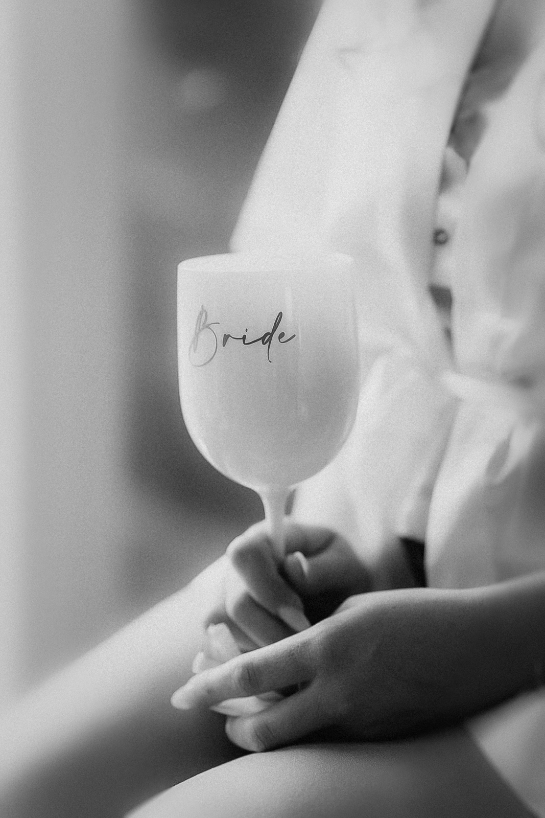 Schwarz-Weiß-Aufnahme: Die Braut hält im Satin-Morgenmantel ein Weinglas mit der Aufschrift „Bride“ in den Händen, ein ruhiger Moment beim Getting-ready in Köln.