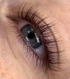 Nahaufnahme eines geöffneten Auges mit blauer Iris und langen, dunklen Wimpern.