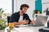 Ein lächelnder Mann mit Headset spricht während einer Videokonferenz am Laptop im hellen Büro.