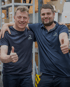 Zwei Männer in blauen Dechra-Shirts mit Daumen hoch im Lager.