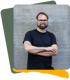 Porträt von Malte: Brille, Bart und schwarzes T-Shirt vor einer grauen Steinwand