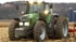Grüner Fendt-Traktor mit leuchtenden Scheinwerfern auf einem braunen Feld mit einer Person am Steuer.