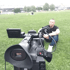 Eine Videokamera filmt einen Mann, der im Gras sitzt.