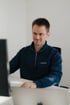 Zwei Männer sitzen in einem modernen Büro und arbeiten an Computern, schwarze Thermoskanne auf dem Schreibtisch.