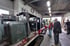 Zwei Männer betrachten eine grüne Diesellokomotive in einer Werkstatt mit weiteren Loks und Werkbänken.