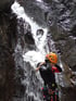 Person in Neoprenanzug und Helm vor einem Wasserfall.