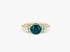 Goldring mit großem blaugrünem Edelstein, flankiert von hellgrünen und weißen Diamanten auf weißem Hintergrund.
