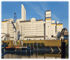 Großer Industriekomplex mit weißen Gebäuden, Kran und blauen Akzenten am Flussufer unter blauem Himmel.