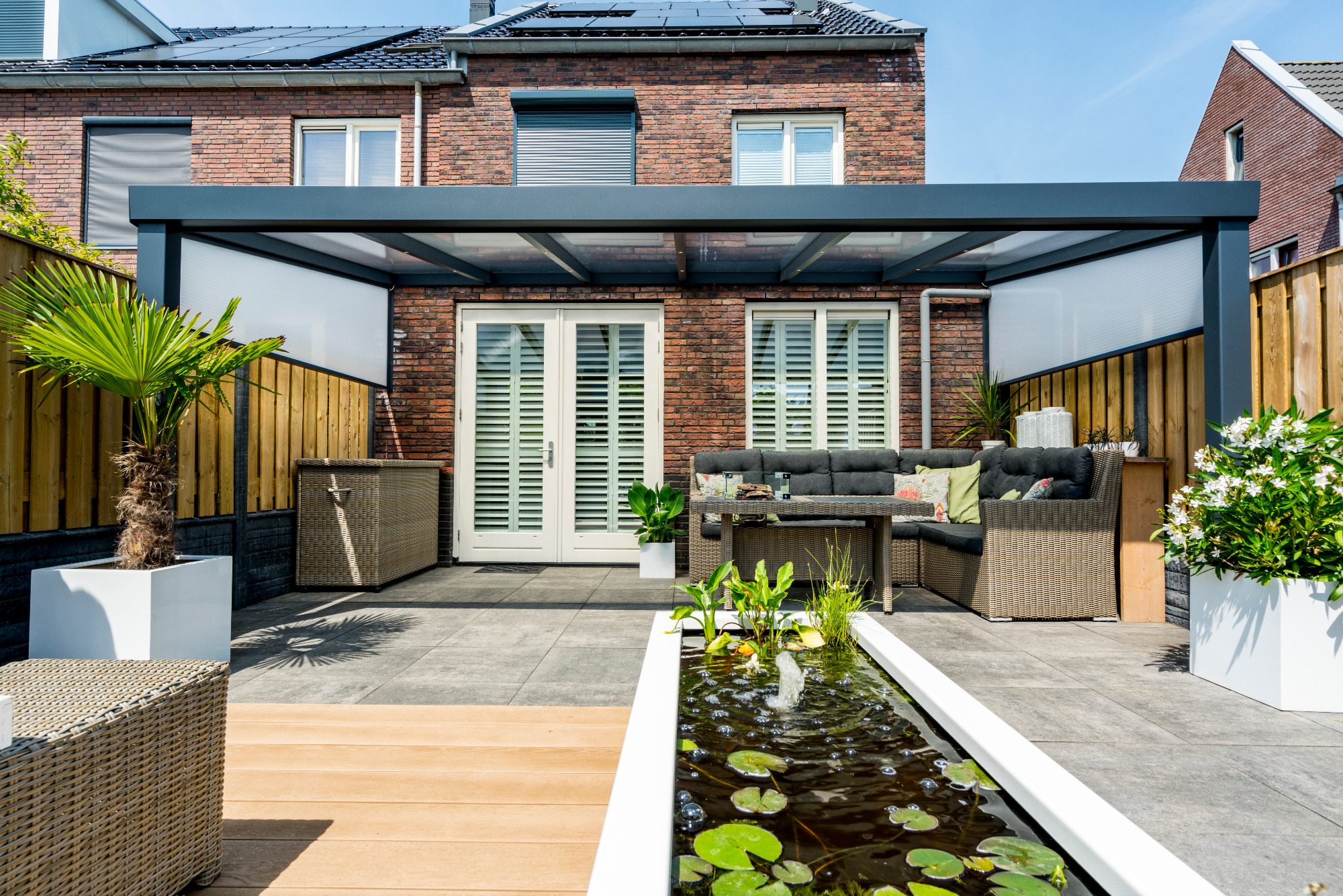 Anthrazitfarbene Terrassenüberdachung mit Glasdach an einem Klinkerhaus