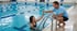 Ein Mann am Beckenrand gibt einem Mädchen im Schwimmbecken ein High-Five.
