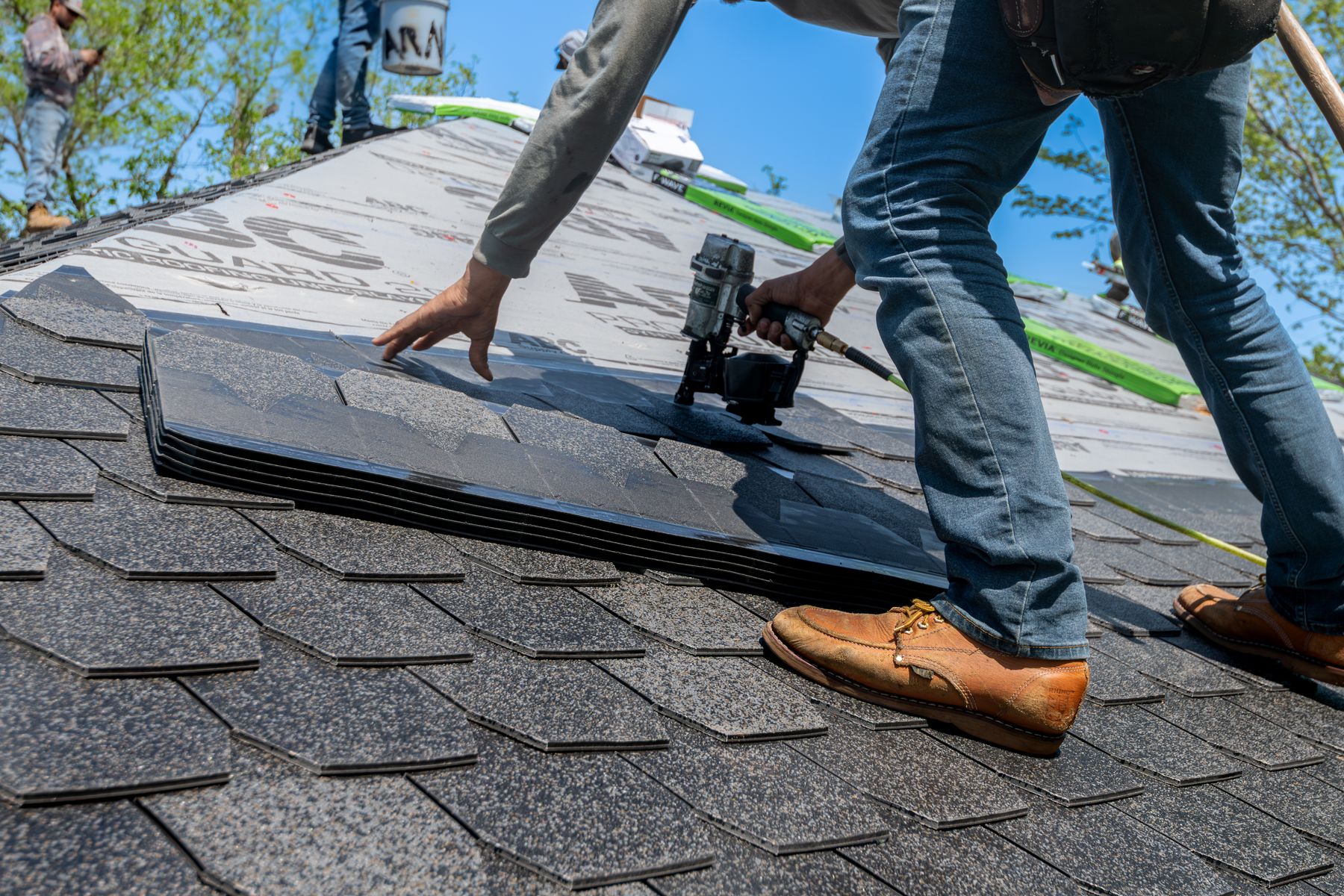Roofer fastening shingles with a nail gun on a residential roof