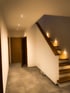 Ein Flur mit Holztüren, Einbaustrahlern in der Decke und einer Holztreppe mit Stufenbeleuchtung.
