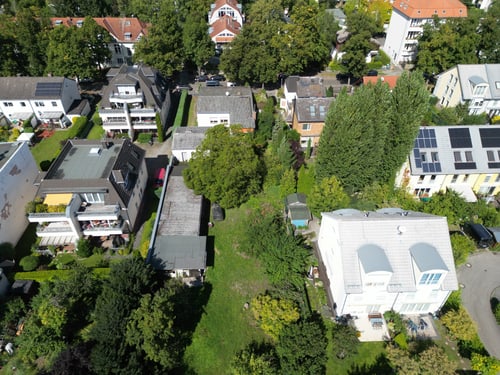 Luftaufnahme von Wohngebäuden und Bäumen in einem Stadtviertel mit Gärten und Solarpaneelen auf Dächern.