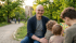 Ein Mann mit Brille lächelt in die Kamera, während er mit drei Kindern im Park sitzt.
