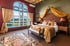 Luxuriöses Hotelzimmer mit Himmelbett, Orientteppich und großem Bogenfenster mit Blick auf einen See und Berge.