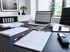 Schreibtisch mit Laptop, Klemmbrett, Taschenrechner, Tablet und Dokumenten in einem modernen Büro.