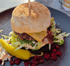 Ein großer Burger mit Käse, Speck und Salat auf schwarzem Teller mit Peperoni und Roter Bete.