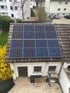 Dach eines Hauses mit 8 Solarmodulen, umgeben von Bäumen und Gebäuden.