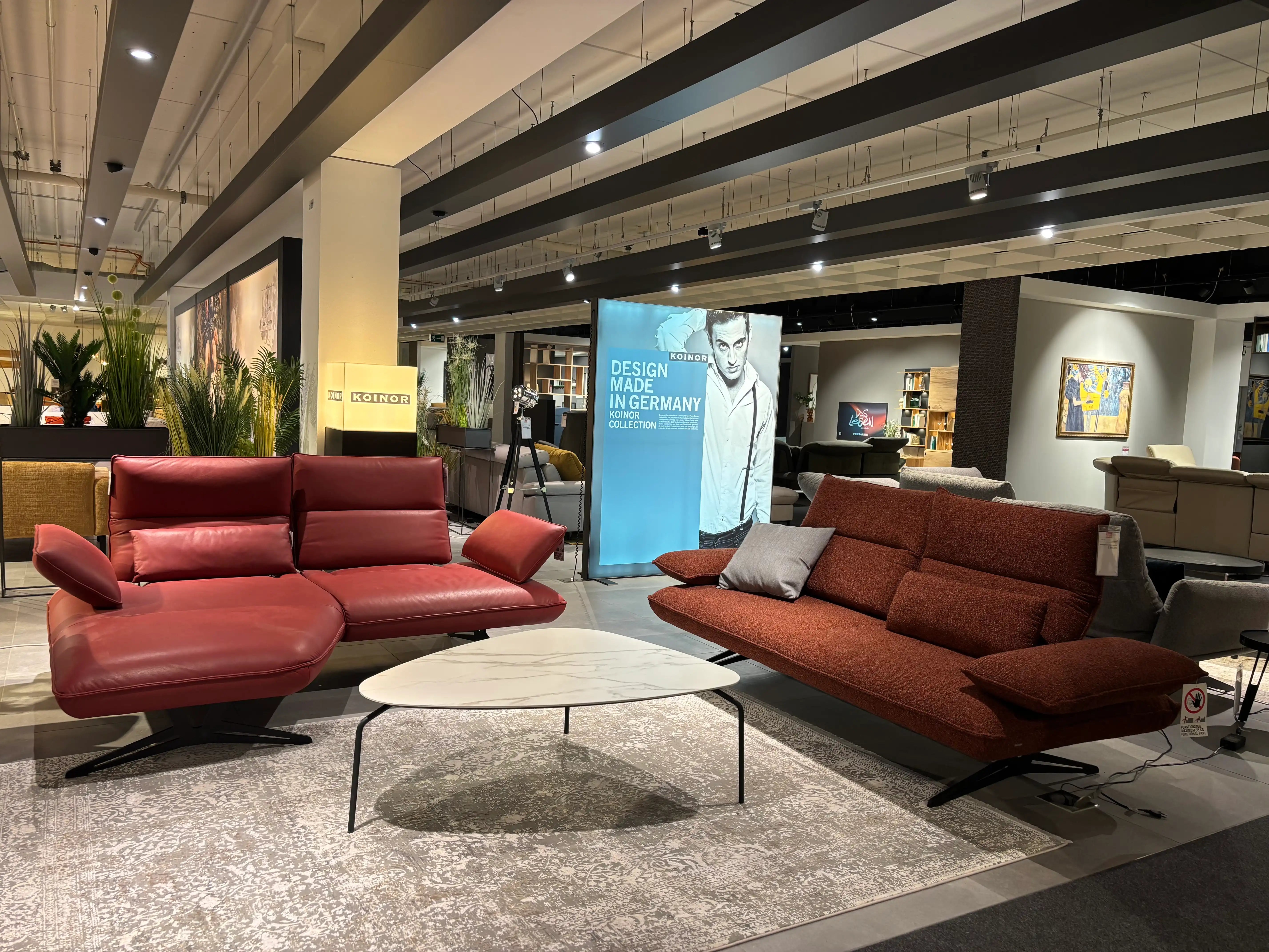 Rotes Koinor-Ledersofa und bordeauxfarbenes Stoffsofa in der Ausstellung von Möbel Graf