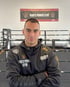 Mann im schwarzen Hoodie mit "KING'S POWER GYM"-Logo steht vor einem Boxring und einem Banner.