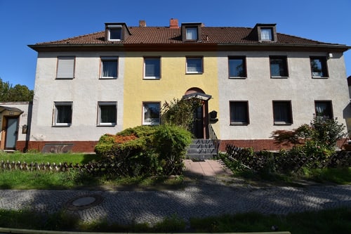 Zweistöckiges Haus mit weißer Fassade und gelbem Mittelteil, umgeben von Grünflächen und einem gepflasterten Weg.