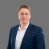 Julian Walter, seriöses Business-Porträt eines Mannes mit Brille im blauen Anzug vor einem neutralen, grauen Hintergrund.