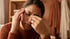 A woman with eyes closed rubs her temple and the bridge of her nose, appearing to experience a headache or sinus pain.