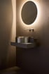 Modernes Badezimmer mit rundem LED-Spiegel, Edelstahl-Aufsatzwaschbecken und Wandarmatur vor dunkler Wand.