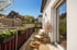Balkon mit Holzmöbeln, Blumenkästen, blühendem Baum und Blick auf Häuser unter blauem Himmel.