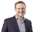 Ein lächelnder Mann mit Brille, blauem Hemd und dunklem Sakko blickt direkt in die Kamera.