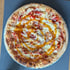 Runde Pizza mit geschmolzenem Käse, roten Paprikastücken, Zwiebeln und einer spiralförmig verteilten orangefarbenen Sauce.