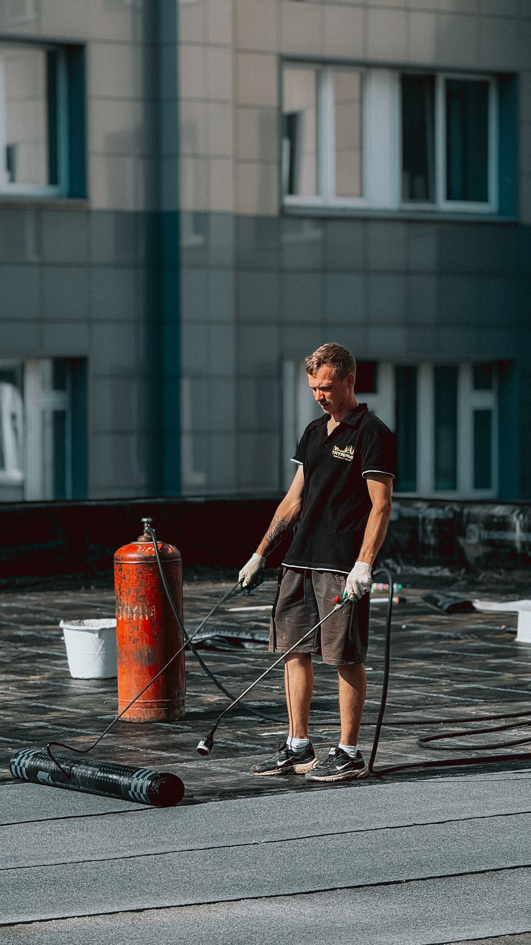 Roofer applying waterproof membrane across a flat commercial rooftop