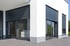 Moderne Hausfassade mit grauen Rollläden vor großen Fenstern und Glastüren.