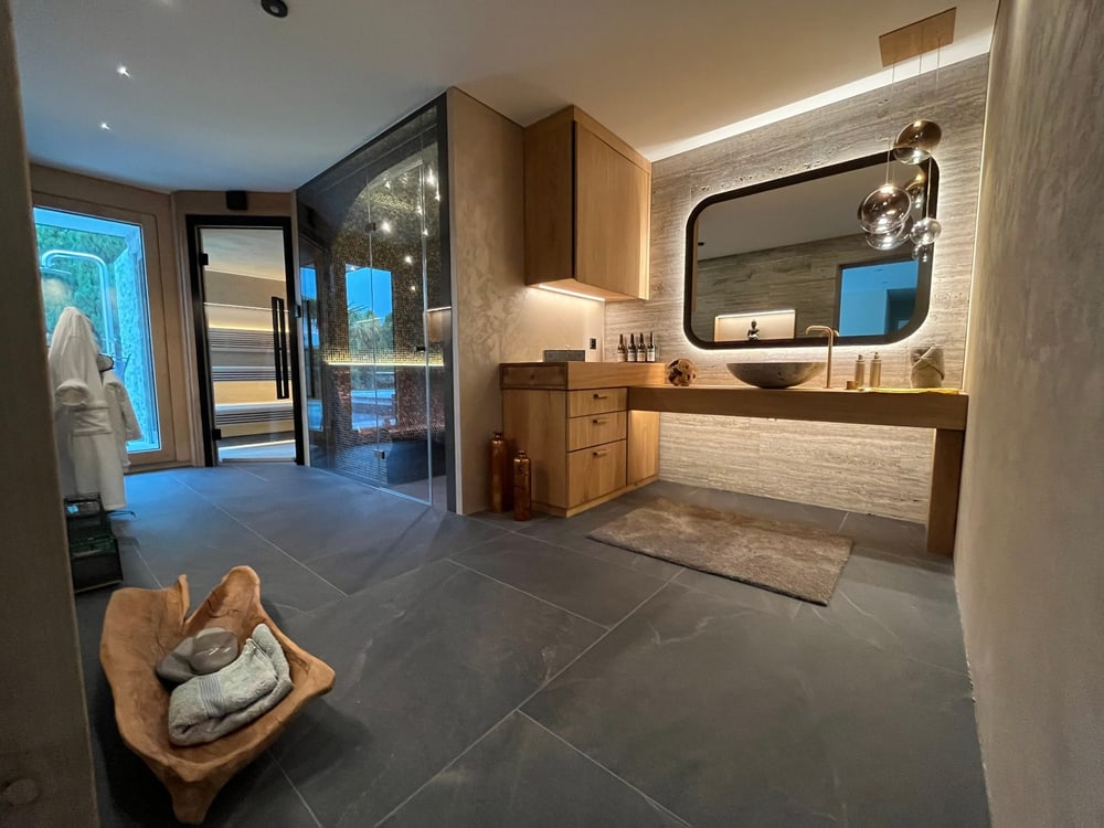 Wellnessraum mit Waschtisch, Spiegel mit Hintergrundbeleuchtung und Blick in Dampfbad und Sauna